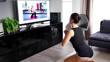 Young woman is doing fitness at home in living room while watching and participating in a class. High quality 4k footage video