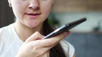 schließen oben Aussicht von jung Frau spricht ein Stimme Botschaft auf ihr Smartphone während Sitzung auf das Couch beim heim. hoch Qualität 4k Aufnahmen video