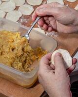 Woman hands are making a damp dumpling. On the wooden counter photo