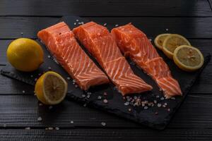 Fresh raw salmon fillet with cooking ingredients, herbs and lemon on black slate photo