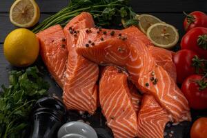 Fresh raw salmon fillet with cooking ingredients, herbs and lemon on black slate photo