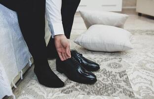 Man in a suit ties up shoelaces on black classic elegant shoes. photo