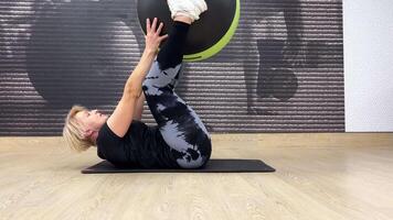 Frau im das Fitnessstudio führt aus Bauch Übungen mit ein passen Ball. Individuell Dehnen auf das Fußboden von geräumig Fitnessstudio mit ihr Beine gestützt oben auf Übung Ball. video