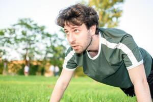 Young man with green t-shirt doing push-ups with gesture of suffering in park photo