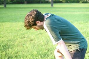 Young man with green t-shirt fatigued and exhausted after doing exercise in park photo