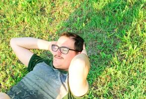 joven hombre con lentes y verde camiseta haciendo Abdominales y hacer ejercicio en parque foto