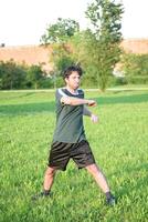 joven hombre con verde camiseta hacer ejercicio y extensión en parque foto