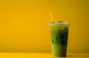 Glass of cold matcha with ice in a plastic cup on a yellow background photo