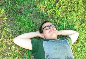 joven hombre con lentes mintió en césped disfrutando vacaciones después estudiando muy contento foto