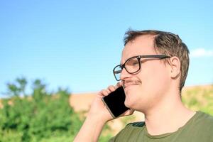 Young man with eyeglasses and green t-shirt talking on cell phone at the park photo