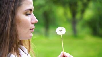 A woman is holding a dandelion in her hand. She is looking at it with a sad expression on her face. video