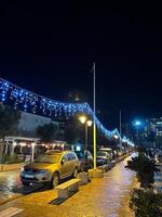 buda, montenegro - 25 diciembre 2022. estacionado carros estar a lo largo el pavimentado la carretera en noche iluminación foto