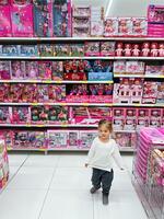 buda, montenegro - 01 noviembre 2023. pequeño niña es caminando mediante un supermercado con muchos muñecas en el estantería foto