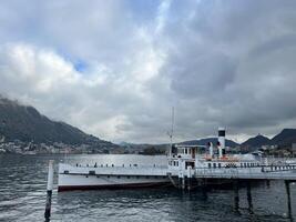como, Italia - 12 noviembre 2023. turista barco soportes a el muelle en el lago en contra el fondo de un alto montaña rango. como, Italia foto