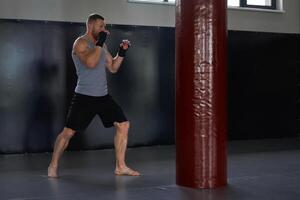 Kickboxer fighting with punch bag in health club photo