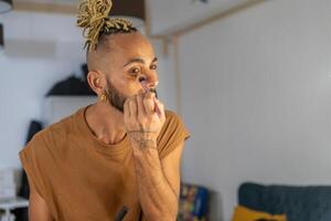 Black brazilian gay applying make up eyeshadow looking mirror photo