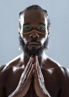 Bearded black gay man with makeup joining hands in blue studio photo