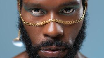 Black gay man with blue eyeshadow and golden accessory on face photo
