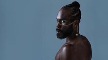 Serious black gay man with light makeup and gold accessory on face photo