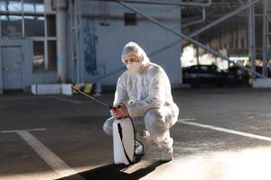 Man dressed white protective overalls spraying surface antibacterial sanitizer sprayer during quarantine photo