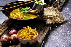 un hembra cocinero adornar su Khao asique kai con un Lima deslizar, Khao asique kai o tailandés tallarines curry con huevo tallarines y pollo palillo de tambor. foto