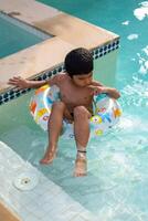 contento indio chico nadando en un piscina, niño vistiendo nadando disfraz a lo largo con aire tubo durante caliente verano vacaciones, niños chico en grande nadando piscina. foto