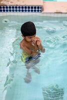 Happy Indian boy swimming in a pool, Kid wearing swimming costume along with air tube during hot summer vacations, Children boy in big swimming pool. photo