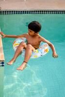 Happy Indian boy swimming in a pool, Kid wearing swimming costume along with air tube during hot summer vacations, Children boy in big swimming pool. photo