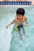 Happy Indian boy swimming in a pool, Kid wearing swimming costume along with air tube during hot summer vacations, Children boy in big swimming pool. photo