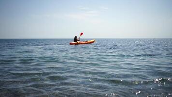 A woman in a pink hat is sitting in a kayak on a calm body of water. The scene is peaceful and serene, with the woman enjoying her time on the water. video