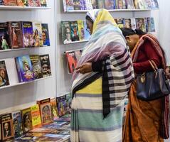 Delhi, India, February 17 2024 - Various age group people reading variety of Books on shelf inside a book-stall at Delhi International Book Fair, Books in Annual Book Fair at Bharat Mandapam complex photo