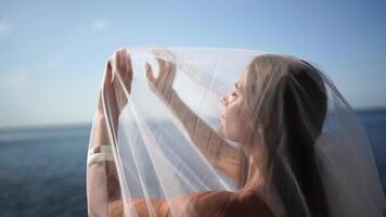 A woman is wearing a veil and standing in front of a blue sky. Concept of elegance and beauty, as the woman is dressed in a white gown and veil. video