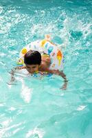 Happy Indian boy swimming in a pool, Kid wearing swimming costume along with air tube during hot summer vacations, Children boy in big swimming pool. photo