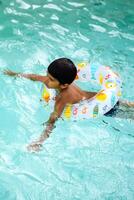 Happy Indian boy swimming in a pool, Kid wearing swimming costume along with air tube during hot summer vacations, Children boy in big swimming pool. photo