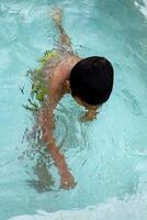 contento indio chico nadando en un piscina, niño vistiendo nadando disfraz a lo largo con aire tubo durante caliente verano vacaciones, niños chico en grande nadando piscina. foto