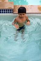 Happy Indian boy swimming in a pool, Kid wearing swimming costume along with air tube during hot summer vacations, Children boy in big swimming pool. photo