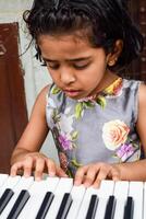 Asian cute girl playing the synthesizer or piano. Cute little kid learning how to play piano. Child's hands on the keyboard indoor. photo