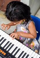 Asian cute girl playing the synthesizer or piano. Cute little kid learning how to play piano. Child's hands on the keyboard indoor. photo