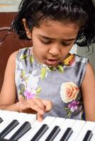 Asian cute girl playing the synthesizer or piano. Cute little kid learning how to play piano. Child's hands on the keyboard indoor. photo