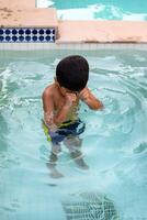 Happy Indian boy swimming in a pool, Kid wearing swimming costume along with air tube during hot summer vacations, Children boy in big swimming pool. photo