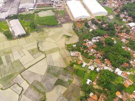 Aerial shot of the village surrounded by large rice fields. Aerial view of settlements in the rice fields in Rancaekek, Bandung - Indonesia. Above. Agriculture Industry. Shot from drone flying photo