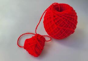 A small ball of red thread and a heart on a white table. photo