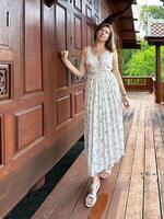 A woman poses thoughtfully by a rich, wooden door, dressed in an elegant floral maxi dress, combining classic architecture with modern style in a serene setting photo