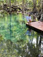 un mujer en un Roca plataforma, rodeado por el lozano verdor de un tropical bosque y el claro aguas de un sereno estanque, reflejando un momento de tranquilidad y conexión con naturaleza foto