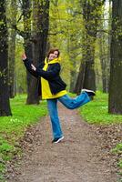 A young woman in a yellow hoodie and blue jeans enjoys a leisurely walk in a lush green park during spring, surrounded by budding trees photo