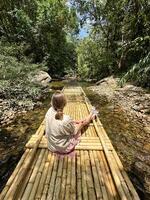 un niña suavemente flotadores abajo un pequeño río en un bambú balsa, inmerso en el tranquilidad de el rodeando selva paisaje foto