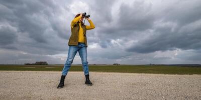 female ornithologist birdman or explorer watches birds with binoculars against a background of a stormy sky photo