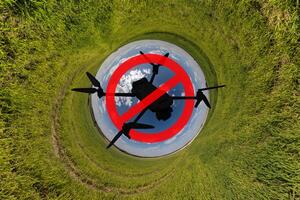 No drone zone sign concept for banning the use of drones in airspace. drone silhouette in red circle with crossed out stripe on blue hole sphere little planet inside grass round frame background photo