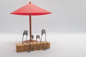 Model safety pin of family sitting on wooden block with red umbrella background. Family insurance concept photo
