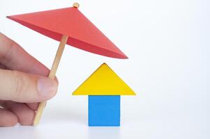 House shape toy covered with red umbrella representing house or property insurance concept photo